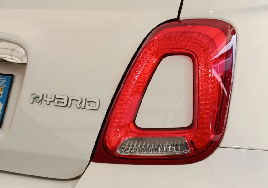 Gros plan sur le feu arrière droit rouge et le logo Hybrid sur la partie arrière blanche d’une Fiat 500 Dolcevita.