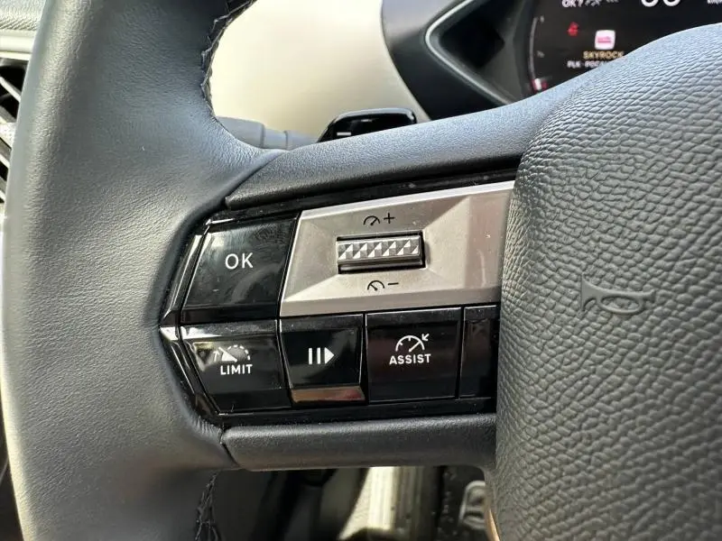 Gros plan sur les commandes au volant gauche du DS3 2024, boutons noirs avec marquages blancs et molette argentée.