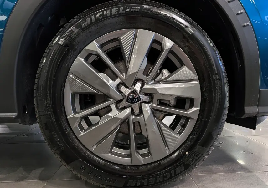 Gros plan sur la jante alliage argentée avec logo Peugeot, montée sur un pneu Michelin, partie avant droite du Peugeot 3008 Bleu Obsession.