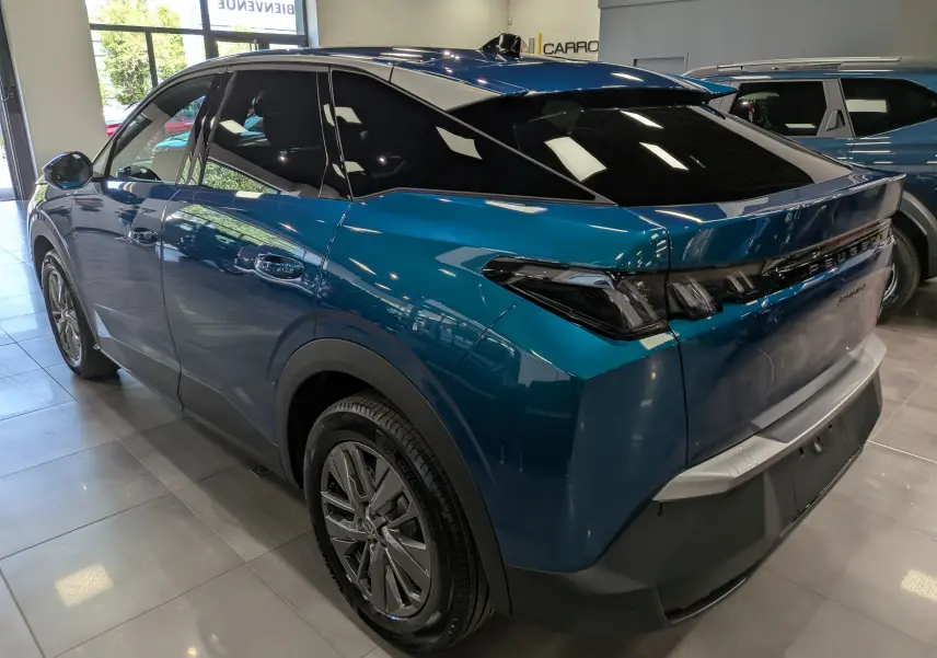 Vue 3/4 arrière droite du Peugeot 3008 Hybrid bleu Obsession avec vitres teintées et jantes alliage en showroom.