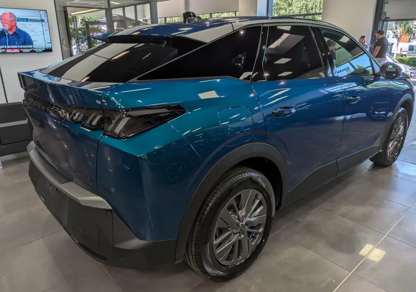 Vue 3/4 arrière droite du Peugeot 3008 Hybrid bleu Obsession avec toit noir et jantes alliage en showroom.