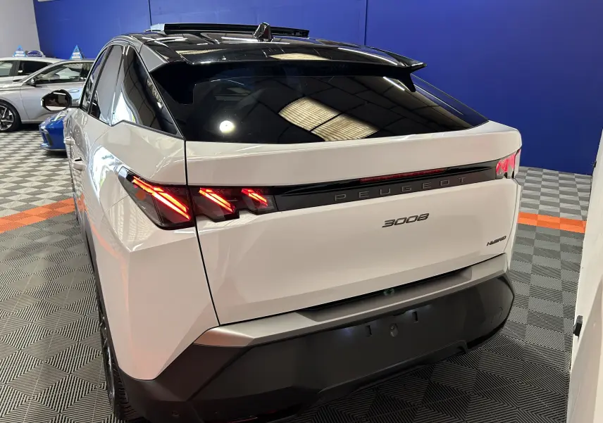 Vue 3/4 arrière droite du Peugeot 3008 Hybrid blanc Okenite avec feux LED allumés et toit panoramique noir.
