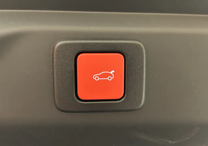 Bouton rouge de commande d'ouverture du hayon sur fond noir, intérieur du Peugeot 3008 Hybrid 2026.