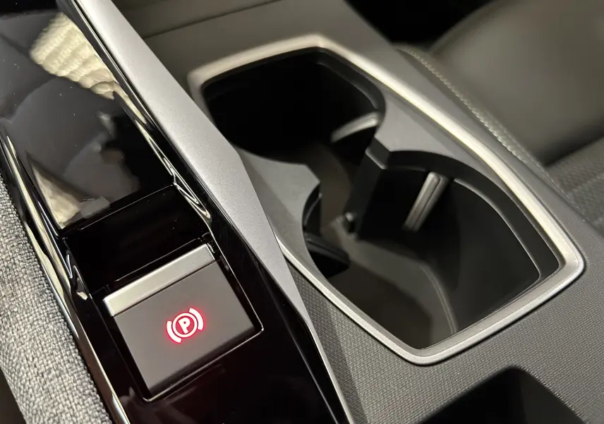 Gros plan sur la console centrale noire et grise du Peugeot 3008 Hybrid avec bouton de frein à main électronique illuminé en rouge.