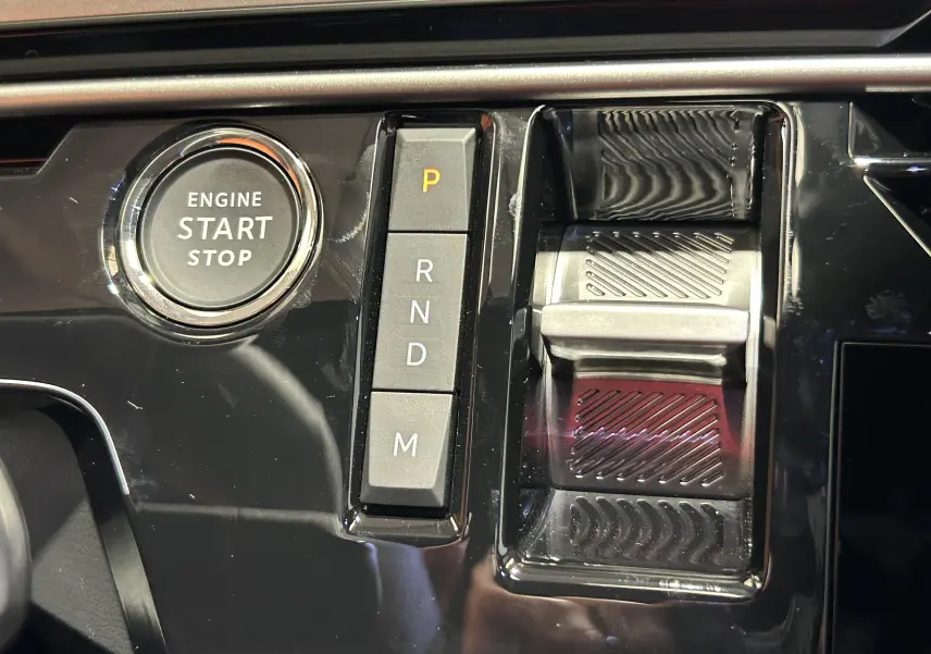 Gros plan sur la console centrale noire brillante du Peugeot 3008 Hybrid avec bouton start/stop et sélecteur de vitesses à boutons.