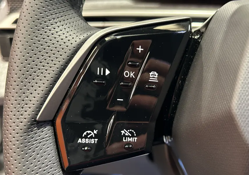 Gros plan sur les commandes noires du volant perforé du Peugeot 3008 blanc Okenite, version Hybrid GT 2026.
