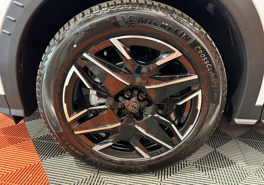 Gros plan sur la roue avant droite du Peugeot 3008 Hybrid blanc, jante alliage noire et chrome avec pneu Michelin CrossClimate.