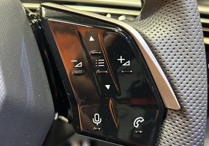 Gros plan sur les commandes au volant perforé du Peugeot 3008 III Hybrid blanc, boutons de volume et téléphone visibles.