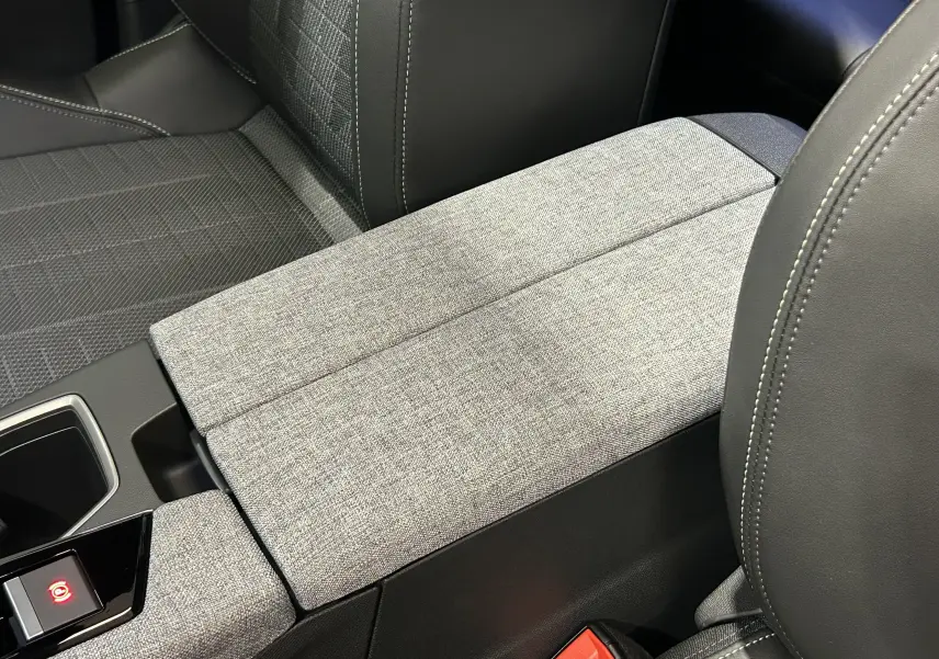 Détail de l'accoudoir central tissu gris et cuir noir dans l'habitacle du Peugeot 3008 Hybrid 2026.