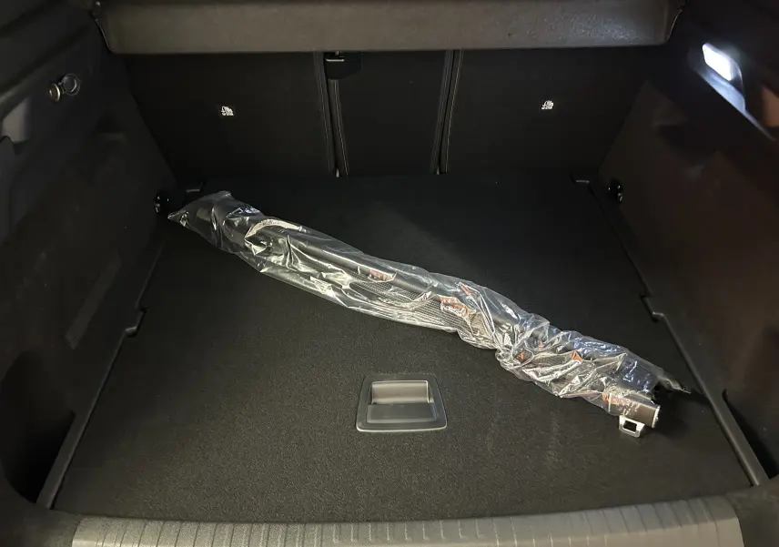Coffre du Peugeot 3008 Hybrid blanc, vue intérieure montrant un accessoire emballé posé sur le tapis noir.