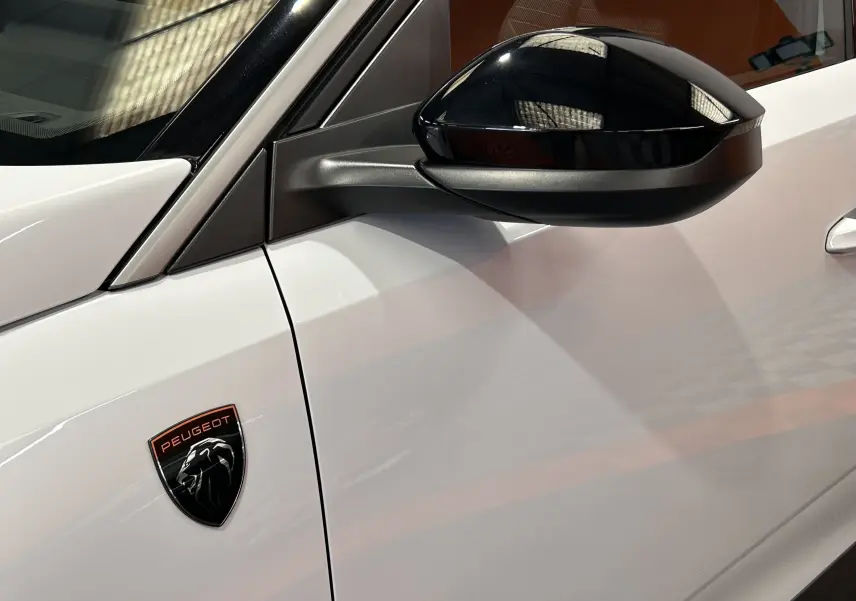 Détail du côté gauche blanc Okenite du Peugeot 3008 III Hybrid avec rétroviseur noir brillant et logo Peugeot sur l'aile.