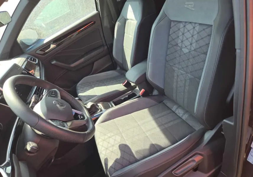 Intérieur avant du Volkswagen T-Roc noir métal 2025, sièges R-Line en tissu et microfleece avec logo brodé.