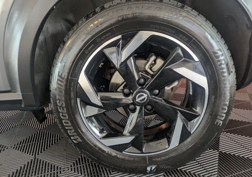 Gros plan sur la roue avant droite du Nissan Juke 2024 gris squale métal, avec jante alliage noire et détails argentés.