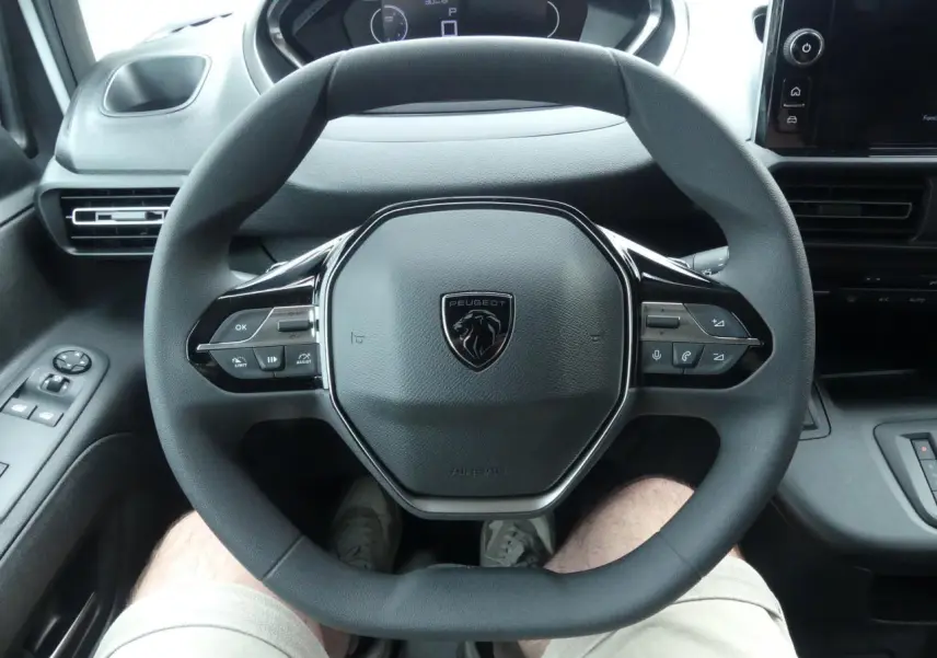 Vue rapprochée du volant multifonctions noir avec logo Peugeot au centre dans l'habitacle du Partner XL blanc 2025.