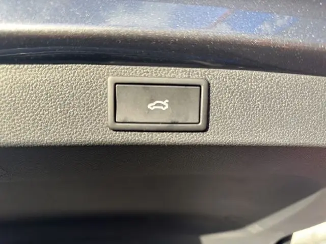 Gros plan sur le bouton noir d'ouverture électrique du coffre du Skoda Karoq gris Graphite, intérieur du hayon visible.