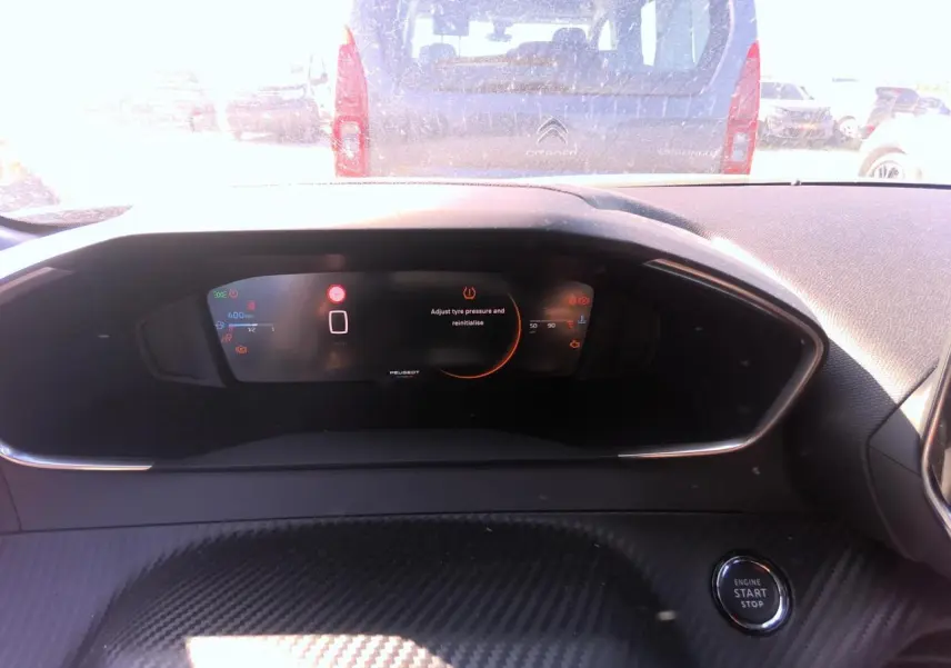 Tableau de bord intérieur noir avec écran numérique Peugeot et bouton start/stop visible en gros plan.