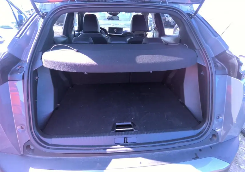Coffre ouvert vu de l'arrière d'un Peugeot 2008 gris clair, avec cache-bagages et intérieur noir visible.
