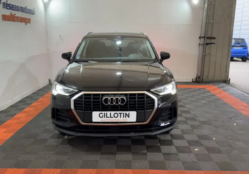 Audi Q3 noir vue de face dans un garage, avec calandre hexagonale chromée et phares LED allumés.