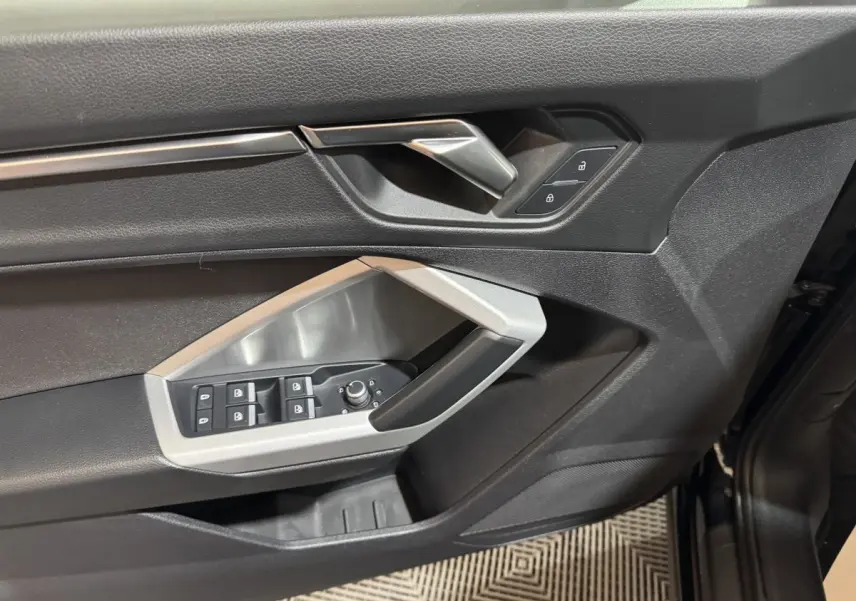 Gros plan sur la porte avant gauche noire de l'Audi Q3 35 TFSI avec commandes de vitres et serrure intégrées.
