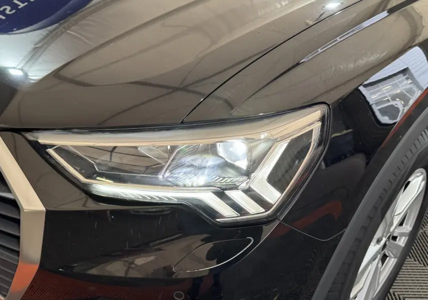 Gros plan sur le phare avant droit du SUV Audi Q3 noir, mettant en valeur son design LED distinctif.