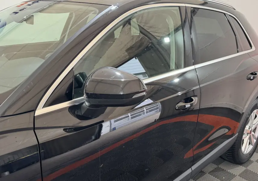 Vue latérale côté gauche d'un Audi Q3 noir brillant avec rétroviseur et poignées de porte visibles.