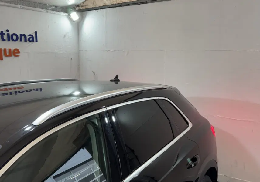 Vue 3/4 arrière côté droit d'un Audi Q3 noir 2022 avec barres de toit chromées et vitres teintées dans un garage.