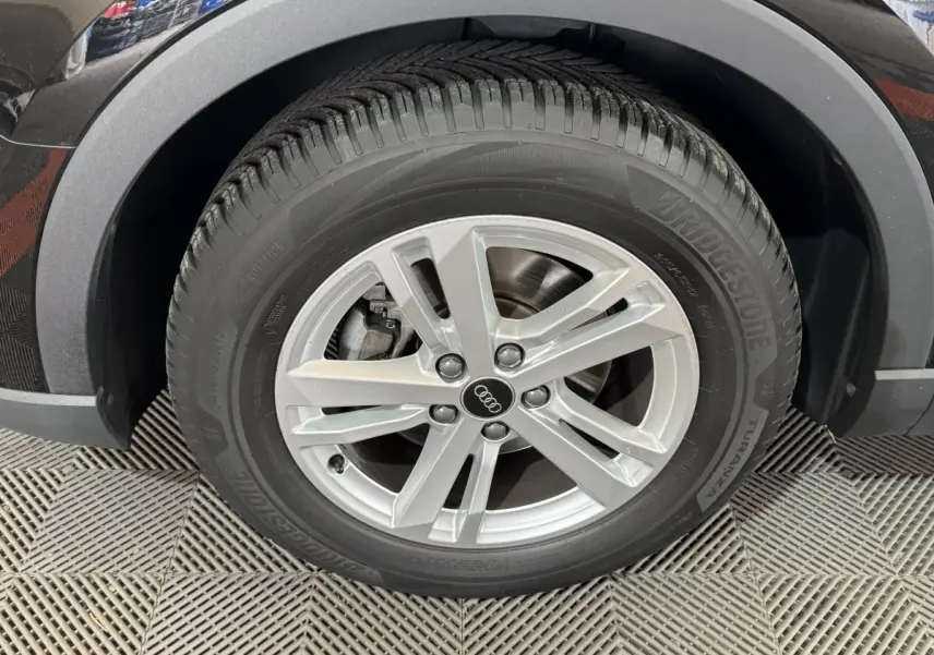 Gros plan sur la roue avant gauche noire de l'Audi Q3 35 TFSI avec jante argentée à 5 branches doubles.