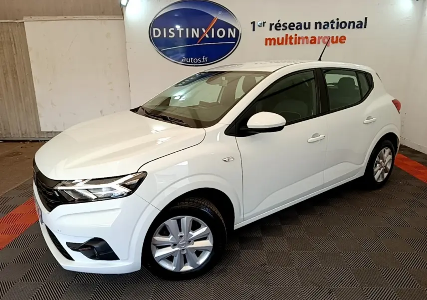 Vue 3/4 avant droit d'une Dacia Sandero Confort TCe 90 blanche, avec phares LED et jantes alliage en intérieur showroom.