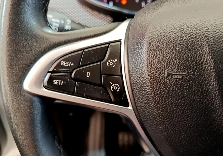 Gros plan sur le côté gauche du volant noir de la Dacia Sandero blanc, avec commandes de régulateur de vitesse.