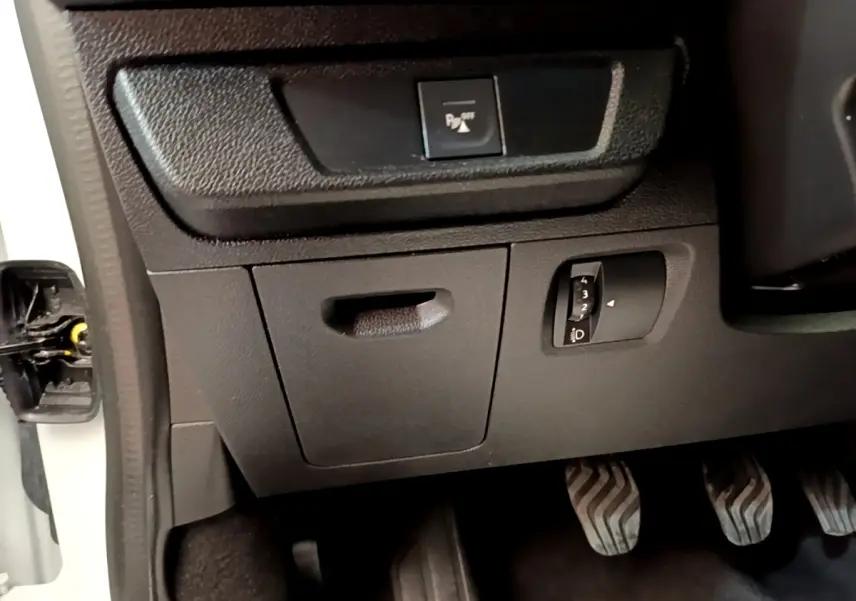 Détail intérieur côté gauche montrant les commandes de réglage des phares et désactivation du système d'aide au stationnement sur Dacia Sandero blanc.