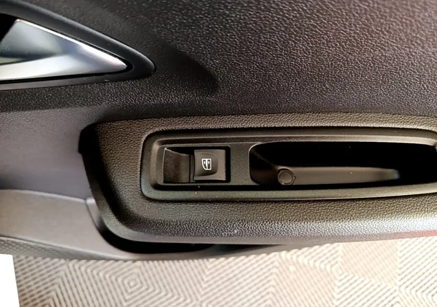 Gros plan sur la commande de lève-vitre noir dans la portière intérieure d'une Dacia Sandero blanche.