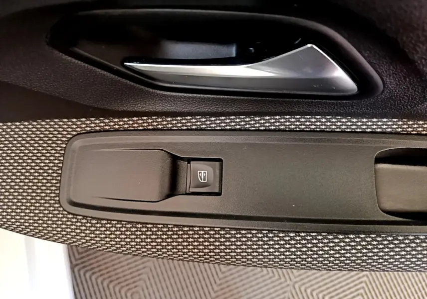 Détail de la commande de lève-vitre côté conducteur sur la porte intérieure d'une Dacia Sandero blanche, tissu gris.