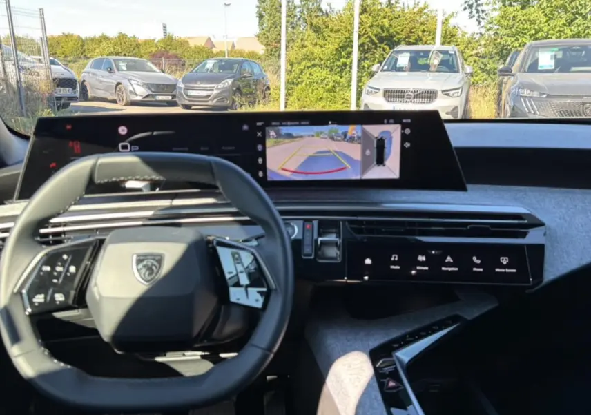 Vue intérieure du tableau de bord du Peugeot 3008 bleu 2025 avec écran tactile et caméra de recul affichée.