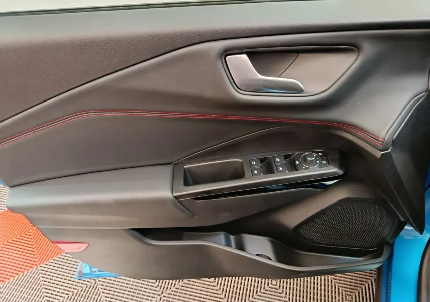 Gros plan sur la porte avant gauche du Ford Puma bleu, avec commandes électriques et surpiqûres rouges visibles.