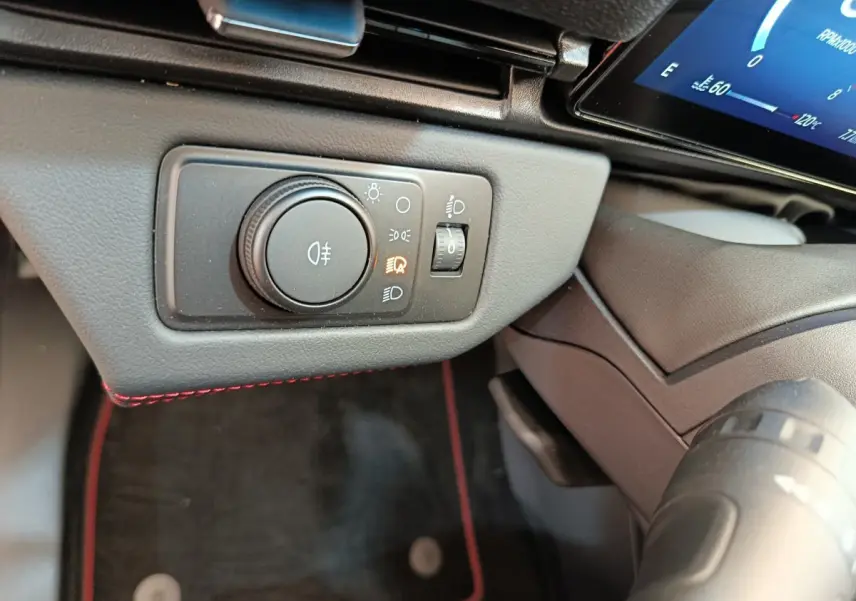 Gros plan sur le bouton de réglage des phares avec éclairage allumé, tableau de bord noir et surpiqûres rouges Ford Puma 2025.