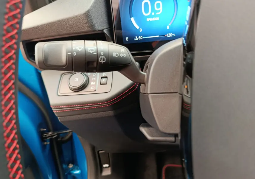 Détail du commodo d'éclairage et tableau de bord numérique du Ford Puma bleu, côté gauche avec surpiqûres rouges.