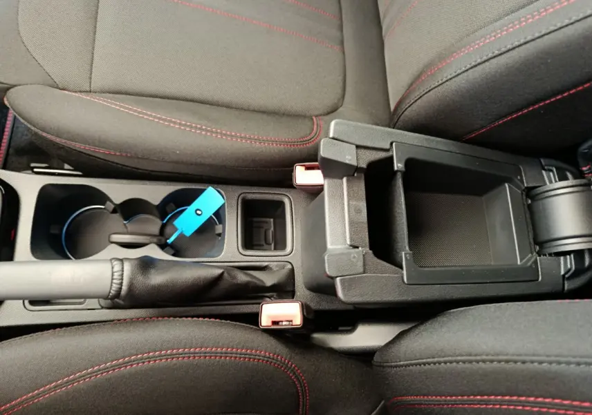 Vue plongeante sur la console centrale noire et les sièges tissu gris foncé avec surpiqûres rouges du Ford Puma 2025.