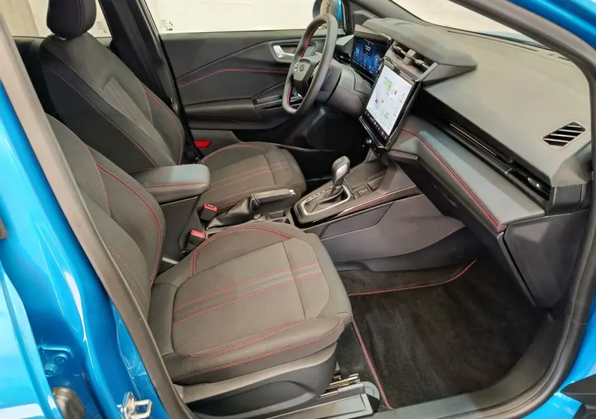 Intérieur avant droit du Ford Puma bleu 2025, sièges noirs avec surpiqûres rouges et tableau de bord digital tactile.