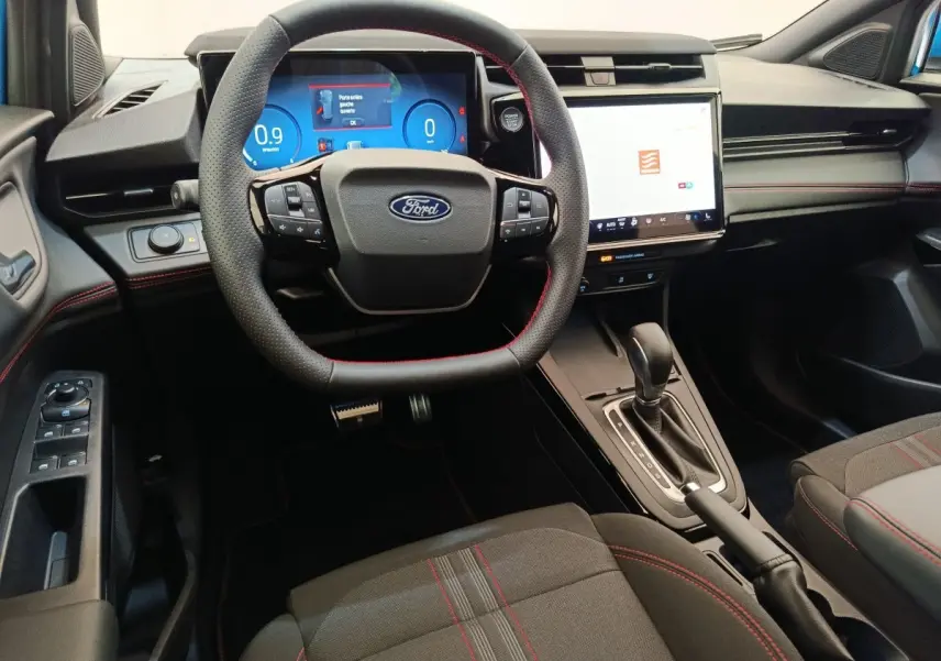 Vue intérieure avant du Ford Puma bleu 2025, volant cuir noir avec surpiqûres rouges et écran tactile central lumineux.