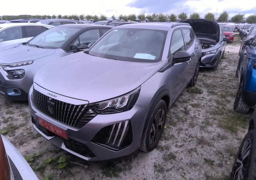 Peugeot 2008 gris clair vue 3/4 avant droit, calandre noire avec marquage vertical et feux LED griffés.