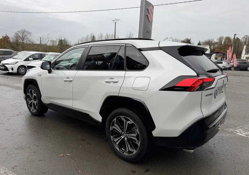 Suzuki Across blanc en vue 3/4 arrière droit, avec jantes alliage noires et toit noir contrasté sur parking.