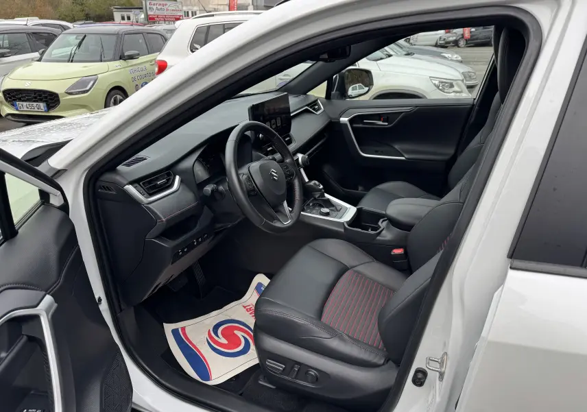 Intérieur côté conducteur du Suzuki Across blanc 2023, sièges noirs avec surpiqûres rouges et tableau de bord moderne.
