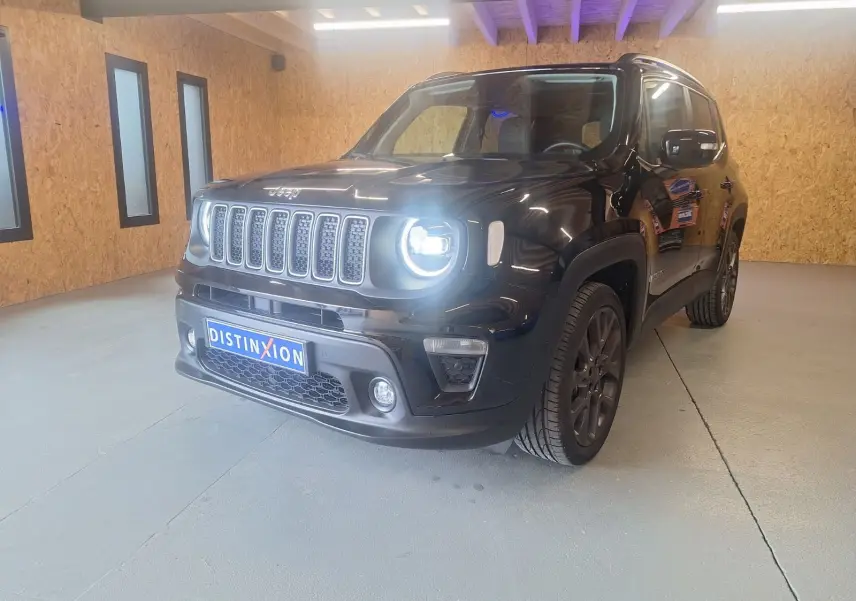 Jeep Renegade noir en 3/4 avant droit, phare allumé, posé dans un intérieur avec murs en bois clair.