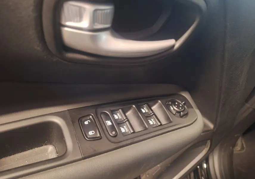 Gros plan sur la commande des vitres et la poignée intérieure côté gauche d’un Jeep Renegade noir 2024.