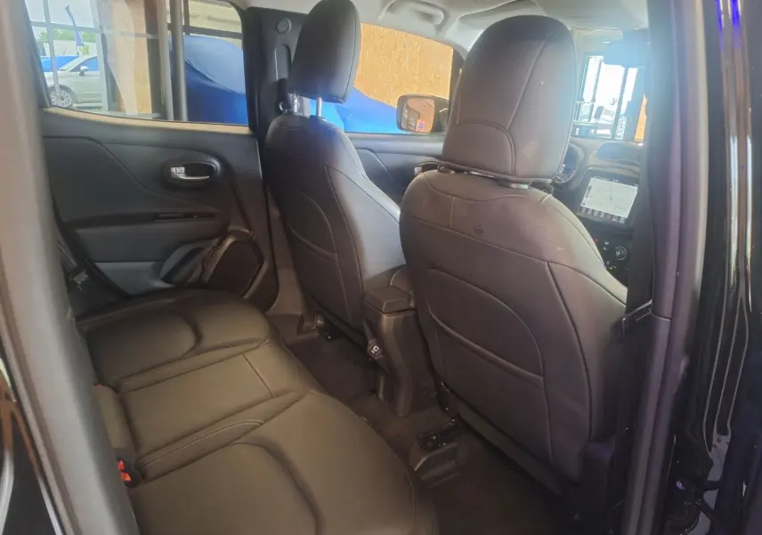 Vue intérieure arrière du Jeep Renegade 2024 noir, sièges en cuir noir et tableau de bord avec écran tactile visible à l'avant.