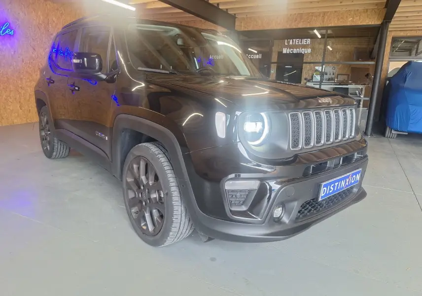 Jeep Renegade noir en 3/4 avant droit avec phares allumés dans un garage moderne.