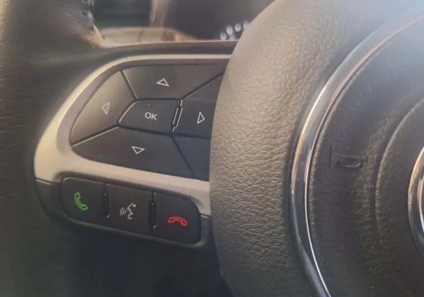 Gros plan sur les commandes multifonctions à gauche du volant noir du Jeep Renegade 2024 hybride.