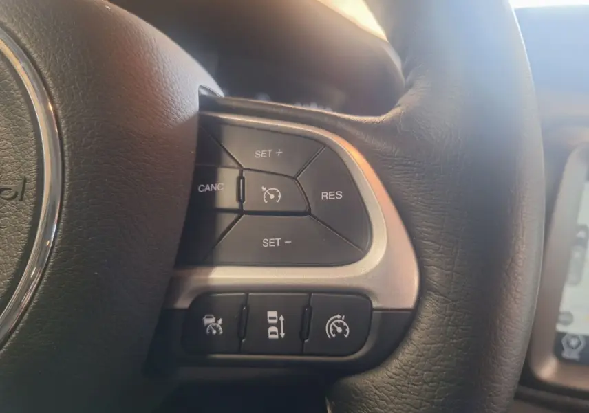 Gros plan sur les commandes de régulateur de vitesse au volant cuir noir du Jeep Renegade 2024 hybride.