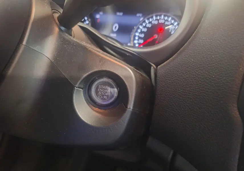 Bouton start/stop moteur en gros plan sur le tableau de bord noir du Jeep Renegade 2024, avec compteurs en arrière-plan floutés.