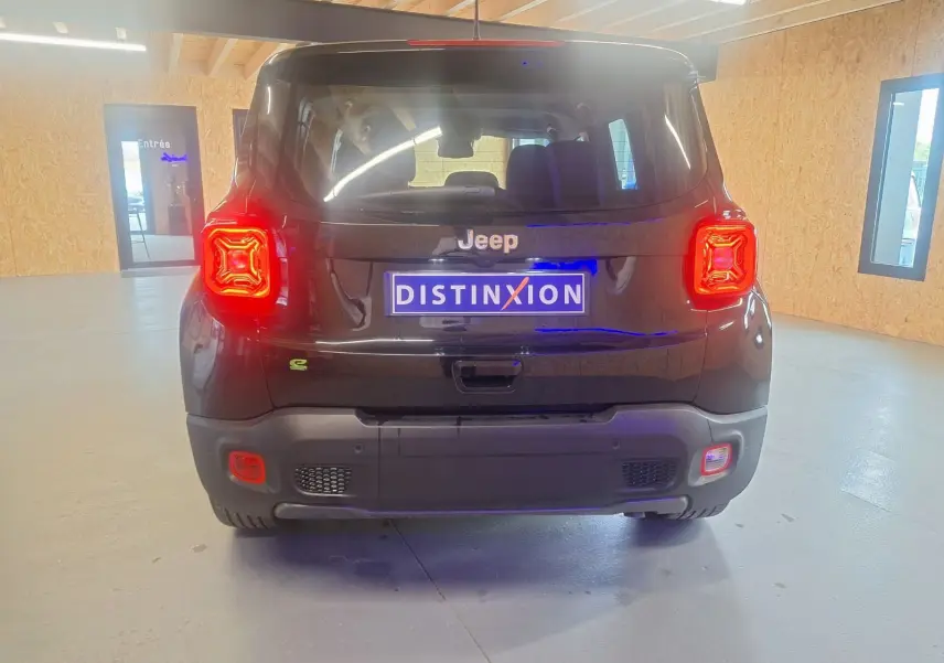 Vue arrière d'un Jeep Renegade noir 2024 avec feux arrière allumés et plaque Distinxion dans un intérieur lumineux.